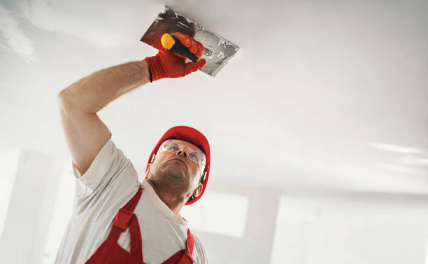 Строительный рабочий в красной форме и шлеме использует штукатурный инструмент на потолке.